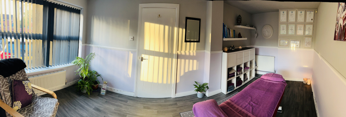 Panoramic view of our treatment room with a massage table in one area and some scented candles burning in the corner